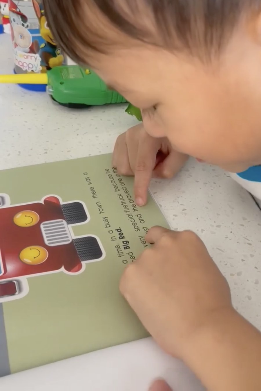 A young child following the words with a finger while reading Big Red