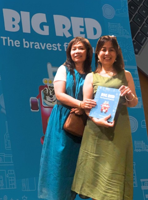 Isel Makapugay holding Big Red at the book signing event, in front of the Big Red banner